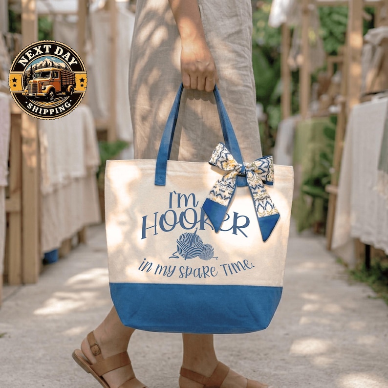 A person is holding a blue and white tote bag with the text "I'm Hooker in my spare time" printed on it.