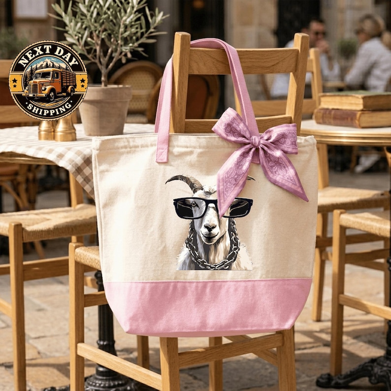 A pink tote bag with a cartoon goat wearing sunglasses and a bow tie, sitting on a wooden chair.