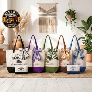 A collection of colorful tote bags with bows, arranged on a wooden floor in front of a wall with a hanging tapestry and potted plants.