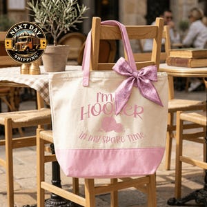 A pink tote bag with the text "I'm Hooper in my spare time" printed on it, sitting on a wooden chair.