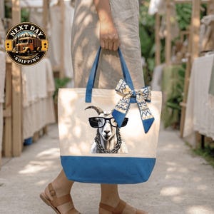 A person is holding a tote bag with a printed image of a goat wearing sunglasses and a bow on it.