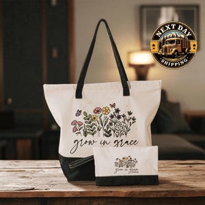 A white tote bag with a floral design and the text " Grow in Grace" printed on it, along with a smaller white bag with a similar floral design and the text " Grow in Grace" printed on it, both placed on a wooden surface.