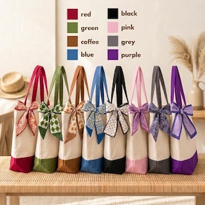 A row of colorful tote bags with bows, each bag displaying a different color and pattern, arranged on a wooden surface.