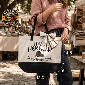 A woman is holding a large tote bag with a humorous text printed on it, standing in front of a market or outdoor setting.