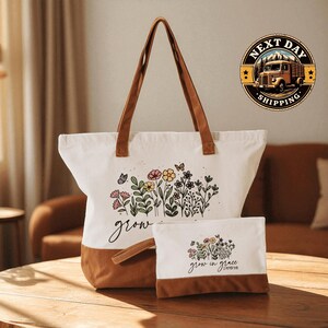 A white tote bag with a floral design and the text "grow in grace" printed on it, along with a smaller white bag with a similar floral design and the text "grow in grace" printed on it, both placed on a wooden surface.