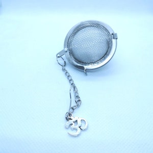 May include: A silver tea infuser with a chain and an Om symbol charm. The infuser is a sphere with a fine mesh.