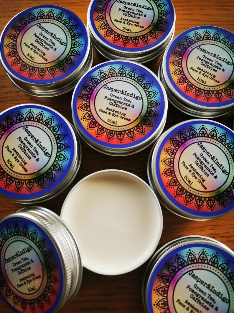 Pu&ograve; includere: Pi&ugrave; contenitori piccoli in argento con etichette colorate che riportano "Jasper & Indigo" e elencano gli ingredienti "T&egrave; verde, melograno e caffeina" e "Crema viso e occhi energizzante" con una dimensione di 50 ml.