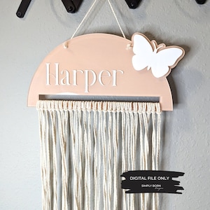 May include: A pink half-circle wooden sign with the name "Harper" in white lettering. A white butterfly is attached to the top right corner of the sign. A white macrame tassel hangs from the bottom of the sign. The sign says "DIGITAL FILE ONLY" and "SIMPLY BORN DESIGNS" in black text.