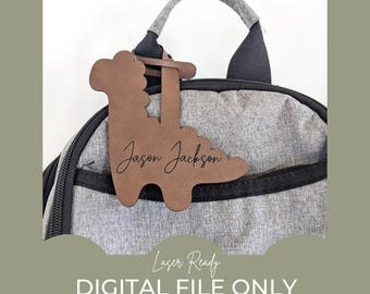 May include: A brown wooden dinosaur-shaped luggage tag with the name "Jason Jackson" engraved on it. The tag is attached to a gray backpack.