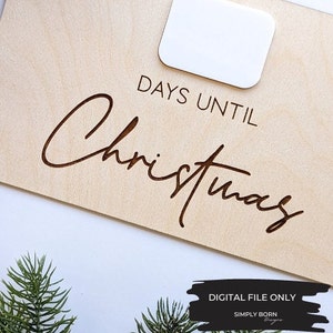 May include: A wooden sign with the text "Days Until Christmas" in a cursive font. The sign has a blank space for a number to be placed. The sign is on a white background.