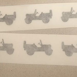 Può includere: Sei adesivi grigi di Jeep sono disposti su due fogli rettangolari bianchi. Ogni adesivo raffigura un profilo laterale di un classico veicolo Jeep, completo di ruote, volante e roll-bar. Gli adesivi sono distanziati uniformemente.