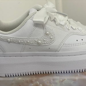 May include: White leather sneakers with a pearl-embellished swoosh and a white satin ribbon tied around the laces.