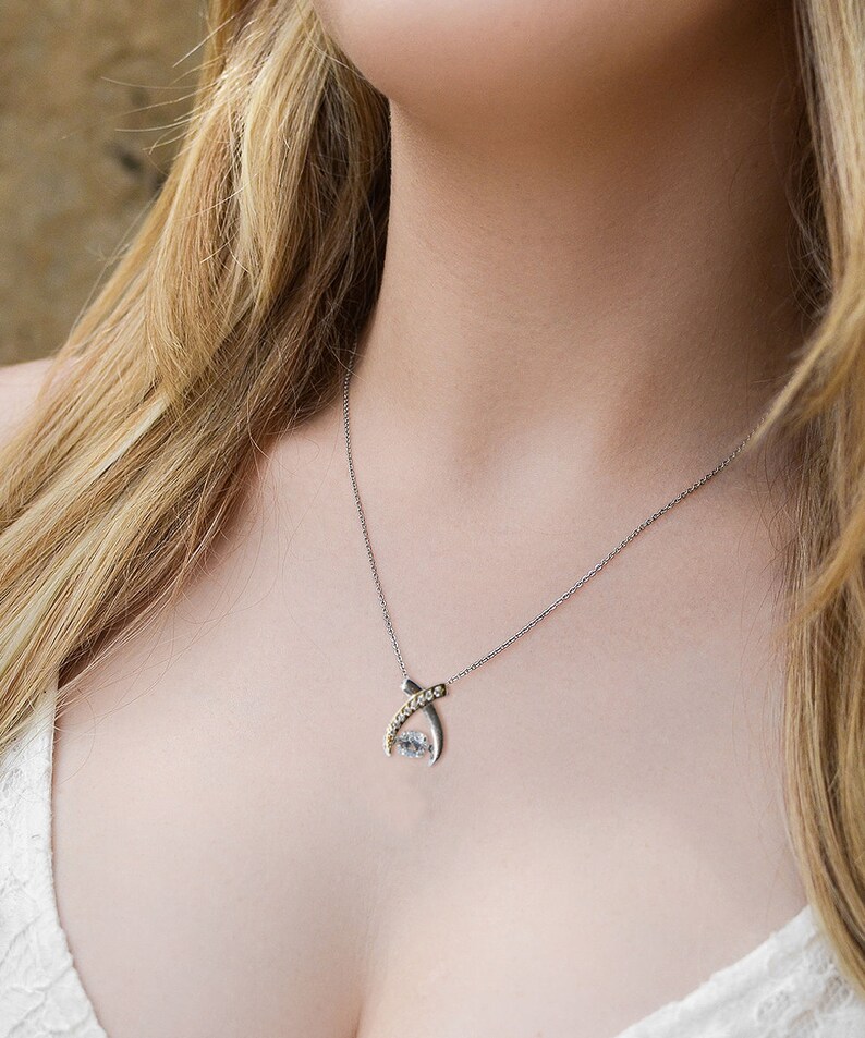 Pode incluir: Um colar de prata com um pingente de cristal transparente. O pingente &eacute; engastado em uma moldura de prata e ouro e tem um design delicado entrela&ccedil;ado.