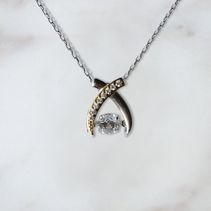 Pode incluir: Um colar de prata e ouro com um pingente de pedra preciosa transparente. O pingente &eacute; rodeado por pedras preciosas menores.