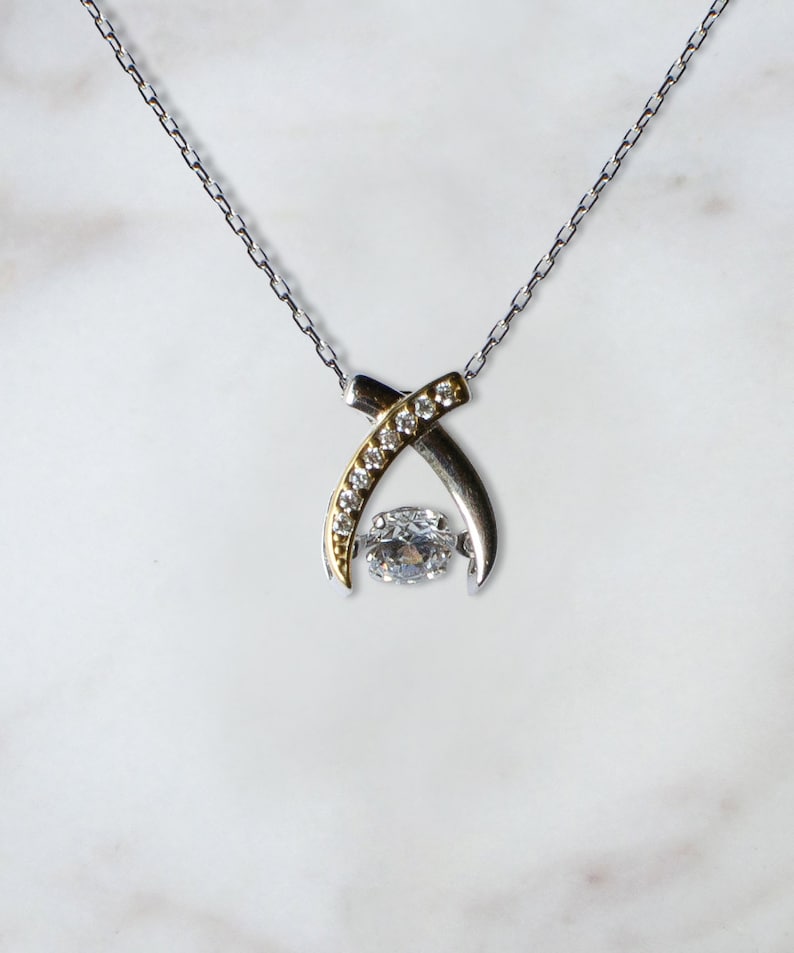 Pode incluir: Um colar de prata e ouro com um pingente de pedra preciosa transparente. O pingente &eacute; rodeado por pedras preciosas menores.
