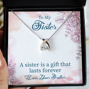 Pode incluir: Um colar de prata com um pingente de cristal transparente e um detalhe dourado. O colar est&aacute; em uma caixa preta com um cart&atilde;o branco que diz "To My Sister" e "A sister is a gift that lasts forever. Love, Your Brother."