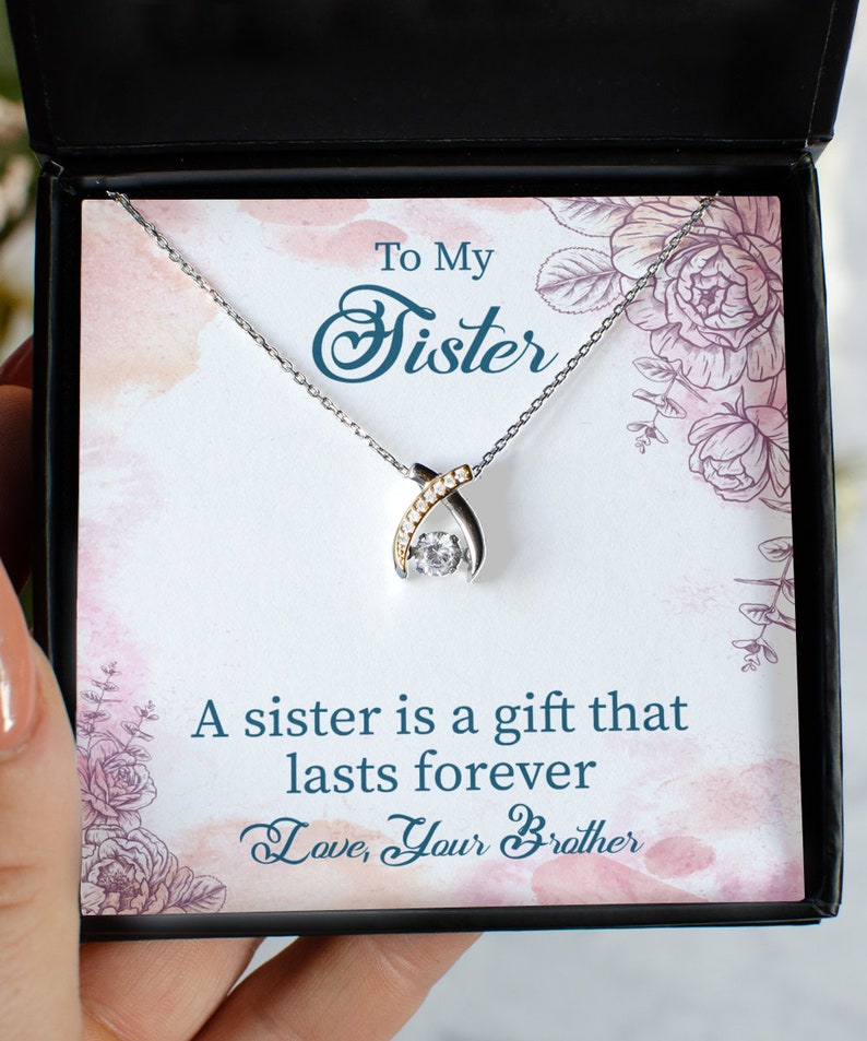 Pode incluir: Um colar de prata com um pingente de cristal transparente e um detalhe dourado. O colar est&aacute; em uma caixa preta com um cart&atilde;o branco que diz "To My Sister" e "A sister is a gift that lasts forever. Love, Your Brother."