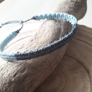 May include: A blue and gray braided bracelet on a wooden surface.