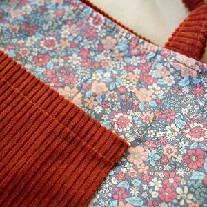 May include: Close-up of a floral patterned fabric tote bag with rust-colored corduroy handles and accents. The floral pattern features pink, blue, and peach flowers on a gray background. The corduroy has a ribbed texture.