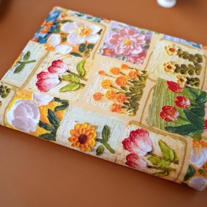Puede incluir: Textil rectangular con estampado floral. El dise&ntilde;o presenta flores bordadas en varios colores, incluyendo tulipanes rojos, cal&eacute;ndulas naranjas y flores blancas. El dise&ntilde;o est&aacute; sobre un fondo beige claro, creando un efecto de patchwork.