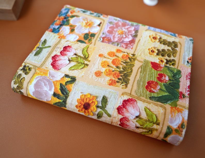 Puede incluir: Textil rectangular con estampado floral. El dise&ntilde;o presenta flores bordadas en varios colores, incluyendo tulipanes rojos, cal&eacute;ndulas naranjas y flores blancas. El dise&ntilde;o est&aacute; sobre un fondo beige claro, creando un efecto de patchwork.