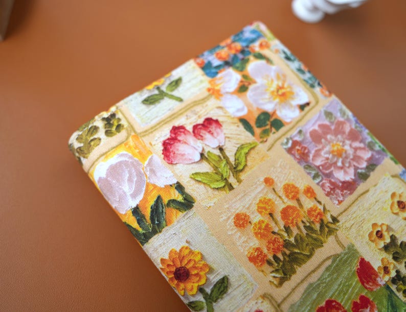 Puede incluir: Primer plano de una tela estampada con flores. El dise&ntilde;o presenta un mosaico de cuadrados con varias flores en tonos rojos, naranjas, amarillos y blancos. Tambi&eacute;n hay hojas y tallos verdes, sobre un fondo beige.