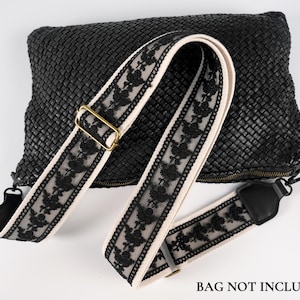 Könnte beinhalten: Eine schwarze geflochtene Handtasche mit abnehmbarem Schulterriemen. Der Riemen besteht aus cremefarbenem Stoff mit schwarzem Blumen-Spitzenbesatz und goldfarbenen Metallbeschlägen. Der Text BAG NOT INCLUDED ist unten im Bild aufgedruckt.