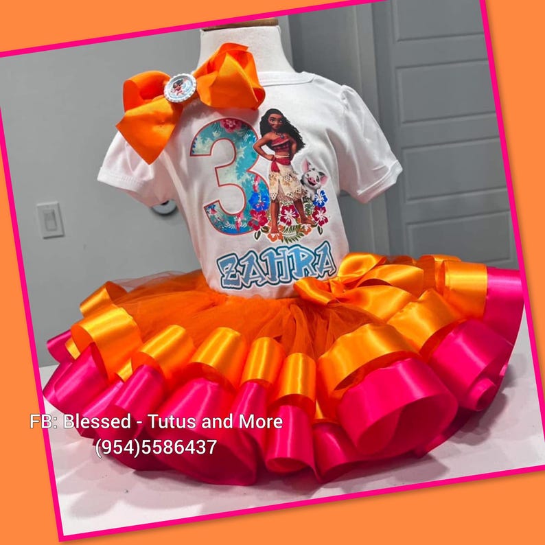 Op de afbeelding: Een wit T-shirt met korte mouwen voorzien van een afbeelding van een personage, het cijfer 3 en de naam ZAHRA, gecombineerd met een oranje en roze gelaagde tule tutu-rok. Een grote oranje haarstrik is bevestigd aan de halslijn van het shirt.
