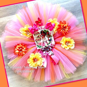 Op de afbeelding: Een meerlaagse tule tutu-rok in roze, oranje en gele tinten, voorzien van een wit grafisch T-shirt met een Moana-personageprint en het cijfer 3. De set is versierd met felroze strikken en grote kunstmatige tropische bloemen.