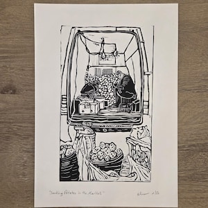 Puede incluir: Grabado en linóleo en blanco y negro titulado "Sorting Potatoes in the Market". La obra de arte representa una escena de mercado con figuras clasificando patatas. Cestas y cajas están llenas de patatas. La impresión es sobre papel blanco.