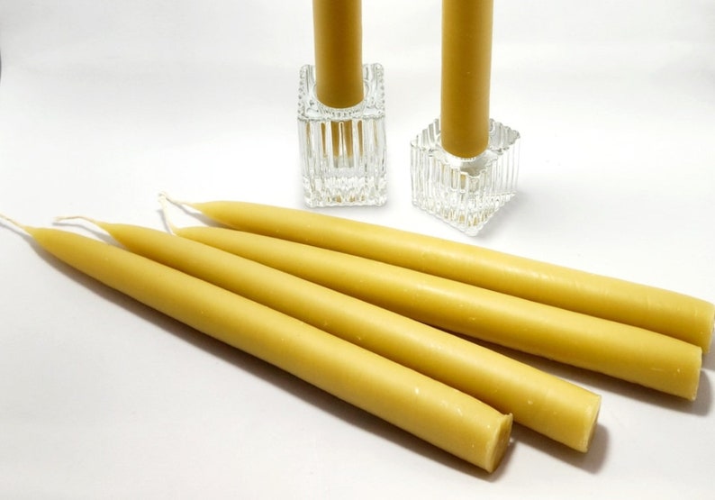 Pu&ograve; includere: Una collezione di candele affusolate gialle, alcune distese e altre in portacandele quadrati di vetro trasparente. Le candele hanno una forma cilindrica liscia e sono di un caldo colore giallo.