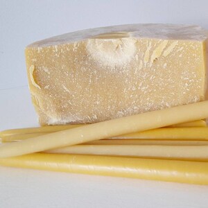 Pu&ograve; includere: Un grande blocco di cera d'api giallo chiaro &egrave; posizionato dietro a diverse candele lunghe e affusolate in cera d'api. Le candele sono di un colore simile al blocco, con una forma cilindrica liscia. Le candele sono lunghe circa 20 cm.