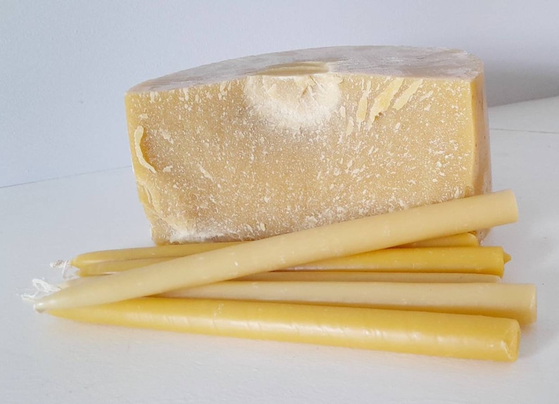 Pu&ograve; includere: Un grande blocco di cera d'api giallo chiaro &egrave; posizionato dietro a diverse candele lunghe e affusolate in cera d'api. Le candele sono di un colore simile al blocco, con una forma cilindrica liscia. Le candele sono lunghe circa 20 cm.