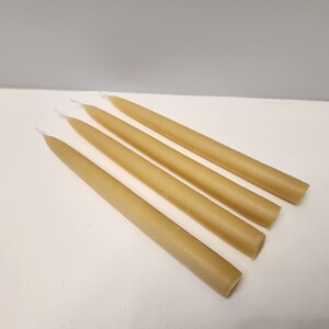 Pu&ograve; includere: Quattro candele affusolate beige disposte diagonalmente su una superficie bianca. Le candele hanno una consistenza liscia e un design classico. Gli stoppini sono visibili nella parte superiore di ogni candela.