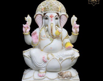 May include: White marble statue of Ganesha, the Hindu god of wisdom and prosperity, sitting on a lotus pedestal with a mouse at his feet. The statue is decorated with gold accents and colorful details.