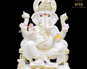 Op de afbeelding: Wit marmeren beeld van Ganesha, de hindoeïstische god van wijsheid en voorspoed, zittend op een troon met een muis aan zijn voeten. Het beeld is versierd met gouden accenten en roze details.