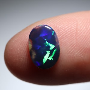 Könnte beinhalten: Ovaler schwarzer Opal-Edelstein mit grünen und blauen Farbschimmern. Der Opal ist in einem Silberring gefasst.