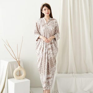 May include: A long, flowing dress with a geometric and floral pattern in shades of brown and white. The dress has a V-neck and three-quarter sleeves. A woman is wearing the dress, with a matching headband.