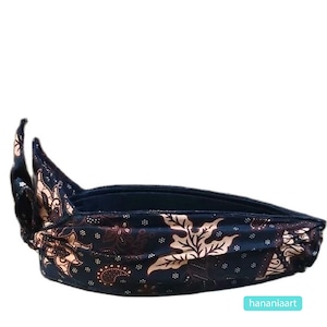 Puede incluir: Un turbante negro y marrón con estampado floral. El turbante está doblado y atado de forma que crea una forma puntiaguda en la parte superior.