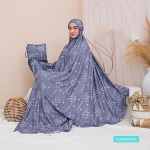 May include: A gray prayer shawl with a white geometric pattern. The shawl is folded and draped over a person's shoulders. The person is wearing a matching headscarf.