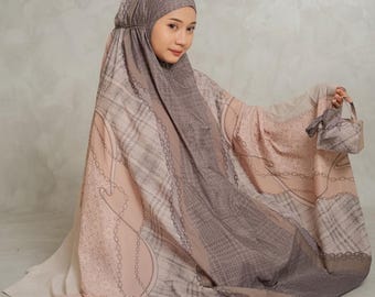 May include: A prayer garment featuring a hood and a flowing silhouette in shades of beige, taupe, and brown. The fabric displays a repeating pattern of chains, plaid, and subtle textures. A matching small fabric bag is held in the right hand.