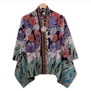Può includere: Un kimono bianco e nero con una stampa floreale e di uccelli colorati. Il kimono ha un bordo dorato e nero e un grande ciondolo d'argento.