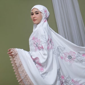 May include: White prayer shawl with pink floral embroidery and lace trim. The shawl is draped over a person's shoulders.