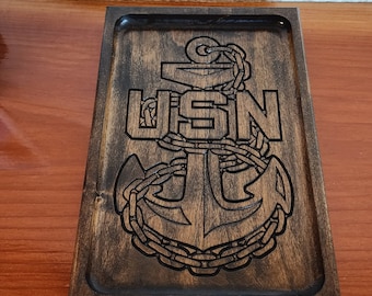 May include: A dark brown wooden tray with a carved US Navy anchor and the letters "USN" in a circle around the anchor.