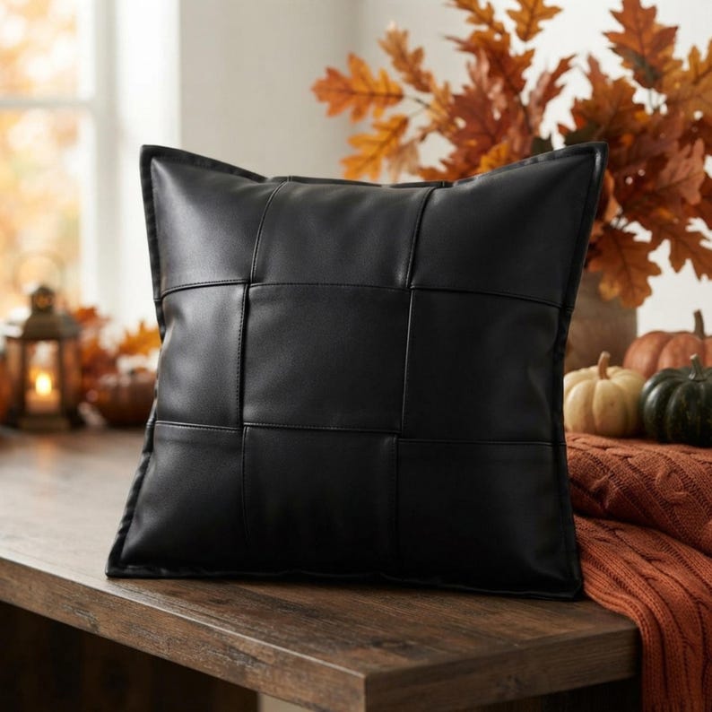 May include: A square throw pillow featuring a black faux leather cover with a woven, basket-weave pattern. The surface consists of wide, interlocking strips of smooth, matte black material that create a grid design across the entire front face.