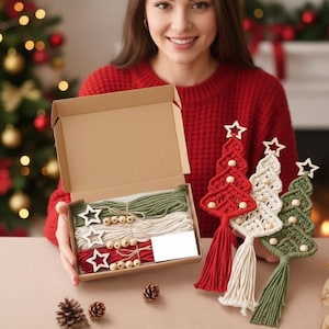 May include: A craft kit with macrame Christmas tree ornaments in red, white, and green. The kit includes twine, wooden beads, and star-shaped wooden cutouts. Finished trees are displayed with tassels and star toppers.