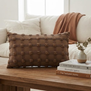 May include: A rectangular brown throw pillow featuring a grid pattern of raised, rounded tufted accents. The pillow has a textured surface with a repeating square design, providing a tactile appearance across the entire front face of the cushion.