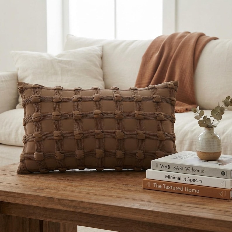 May include: A rectangular brown throw pillow featuring a grid pattern of raised, rounded tufted accents. The pillow has a textured surface with a repeating square design, providing a tactile appearance across the entire front face of the cushion.