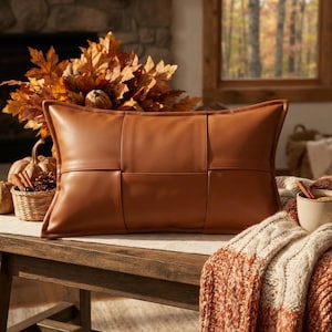 May include: A rectangular cognac-colored faux leather pillow featuring a woven-style panel design with visible stitched seams. The pillow has a smooth, matte finish and a structured rectangular shape, presented as a solid-colored decorative cushion.