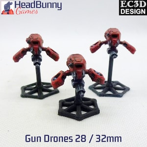 May include: Three red and black painted miniature gun drones on hexagonal bases. The drones are 28mm to 32mm in size. The bases are black and have a hexagonal shape. The drones are painted in a red and black color scheme. The drones are designed for tabletop gaming.